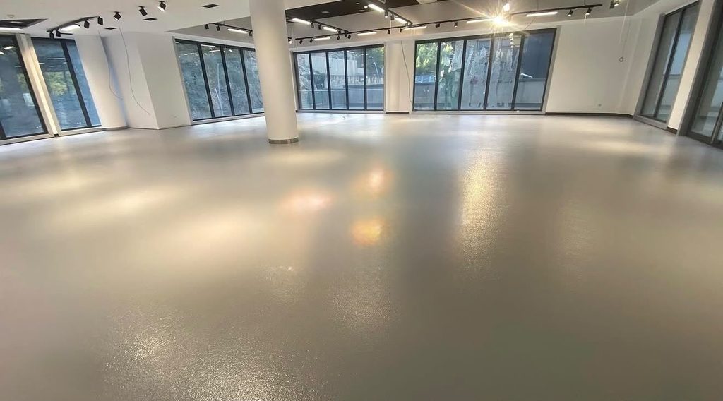 Pavimento continuo de resina claro en un espacio diáfano con ventanas grandes