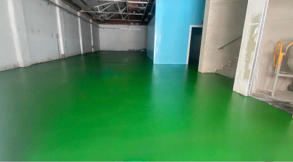 Pavimento de resina verde aplicado en un espacio de trabajo industrial, con superficie continua yacabado liso